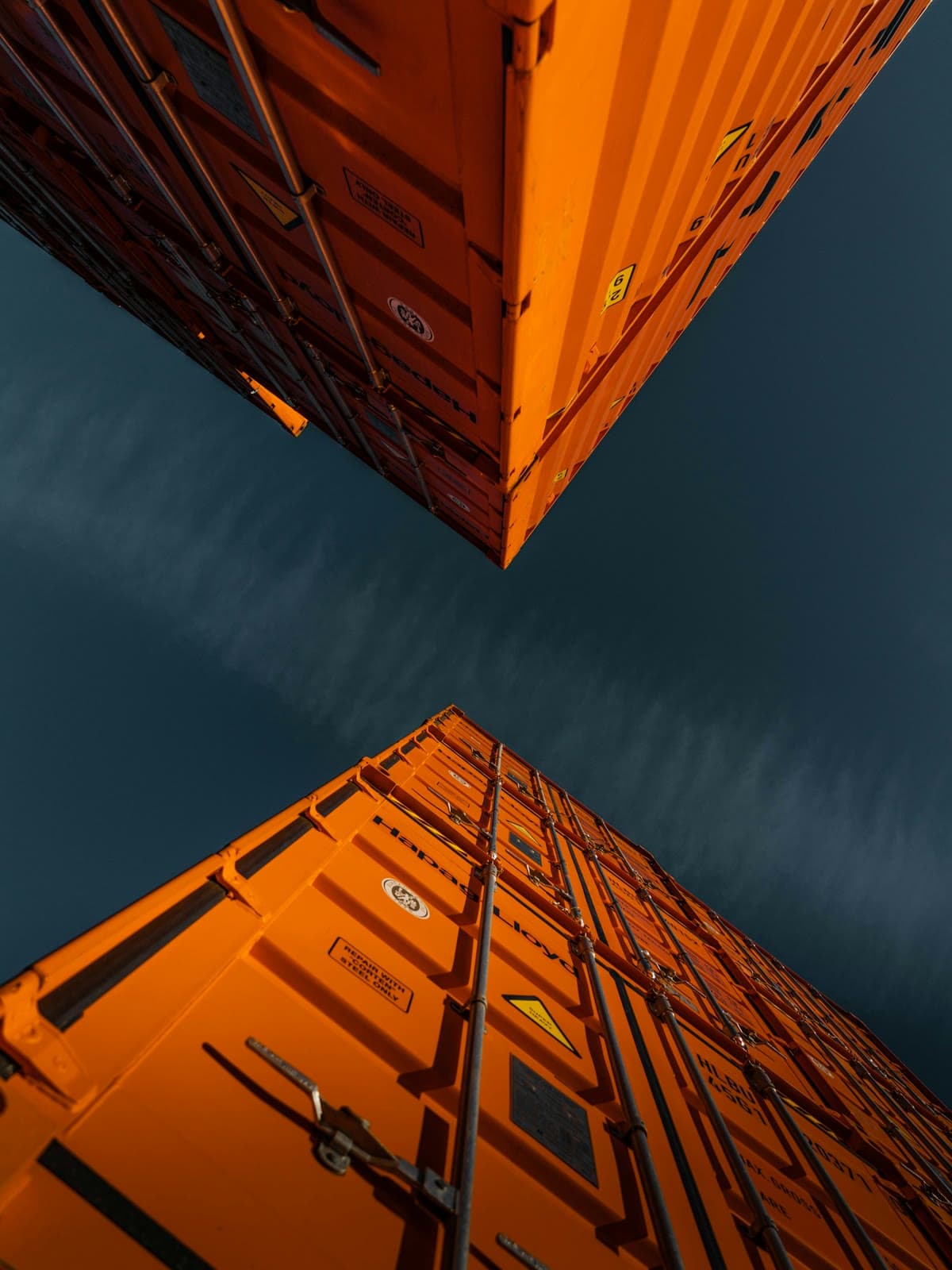 Orange shipping containers rising into a deep blue sky