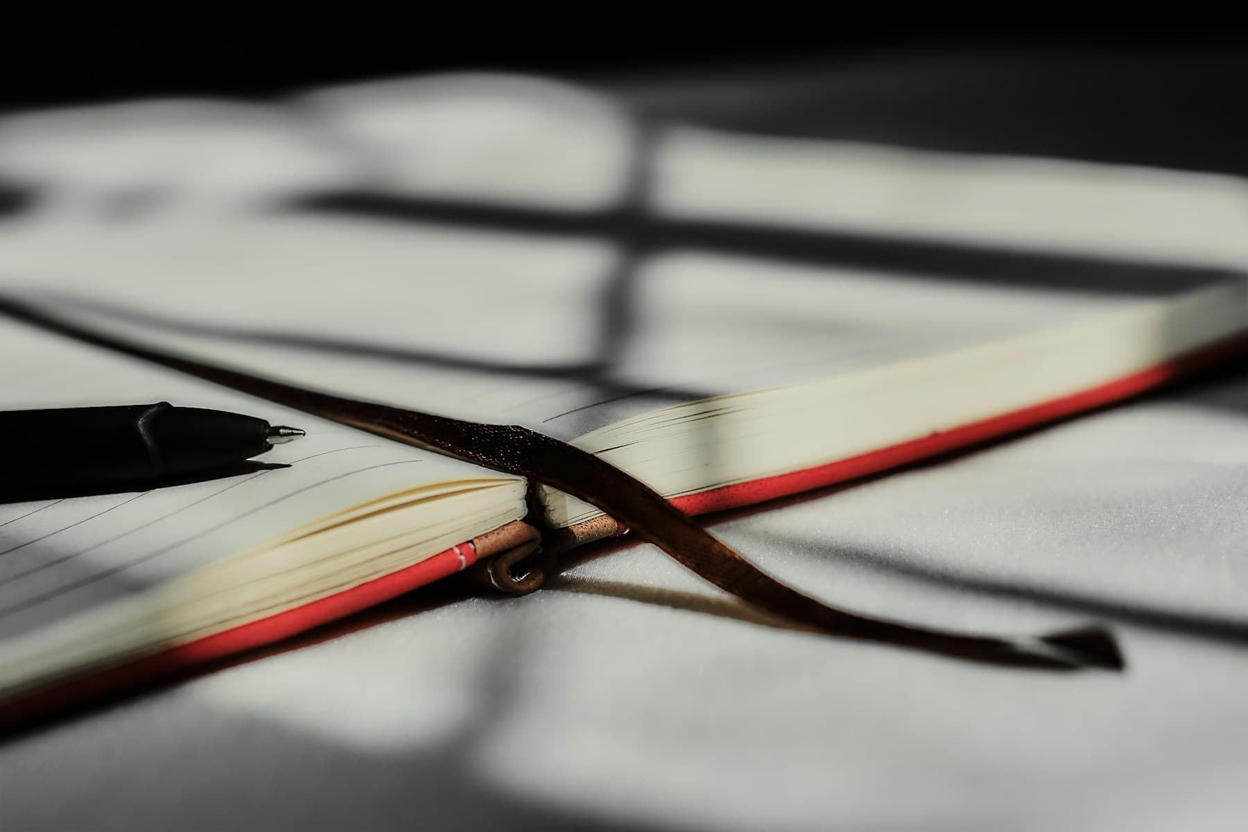 An open book and pen crossed by precise window shadows